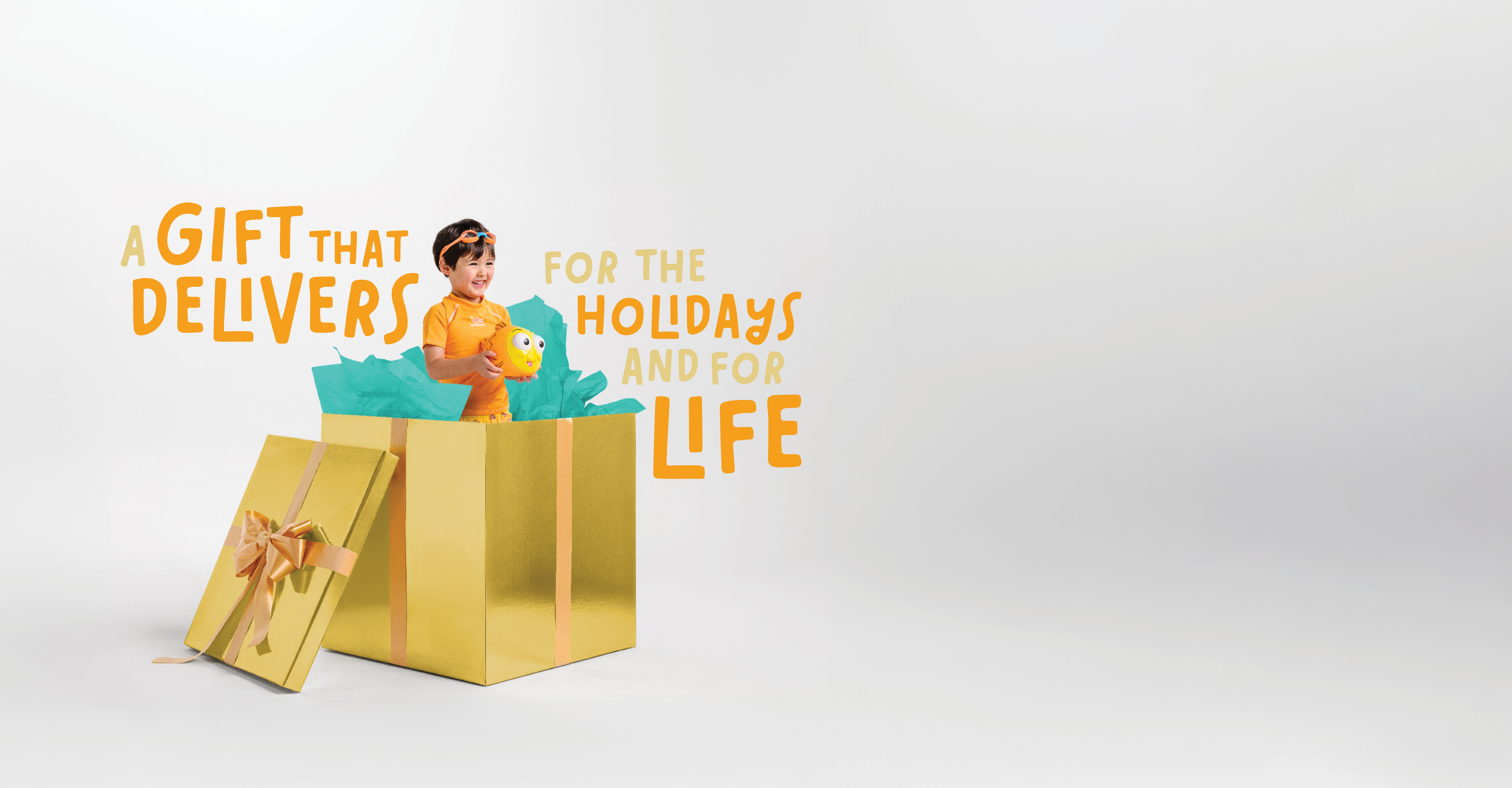 A child in a giant gold gift box holding a goldfish toy, with the words: A gift that delivers for the holidays and for life